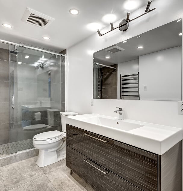 Modern bathroom with white walls, featuring a glass-enclosed shower, sleek vanity with integrated sink, large mirror, and recessed lighting, conveying a clean and minimalist aesthetic.