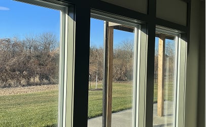Large windows overlook a sunny outdoor scene, with green grass, a wooden pergola, and leafless trees under a clear blue sky, conveying tranquility.