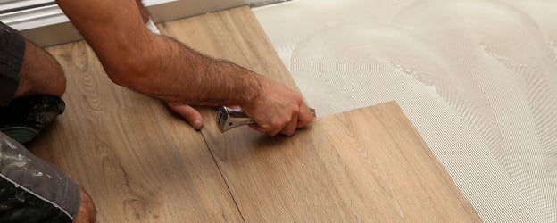 A person installs wooden flooring, using a tool to align planks on adhesive. The image depicts focus and precision in home improvement work.