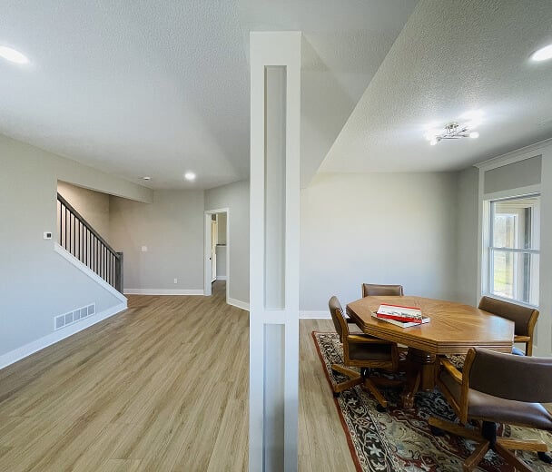 Modern living space with wood flooring, open layout, and neutral walls. A round dining table with chairs on a rug is near a window. Cozy ambience.