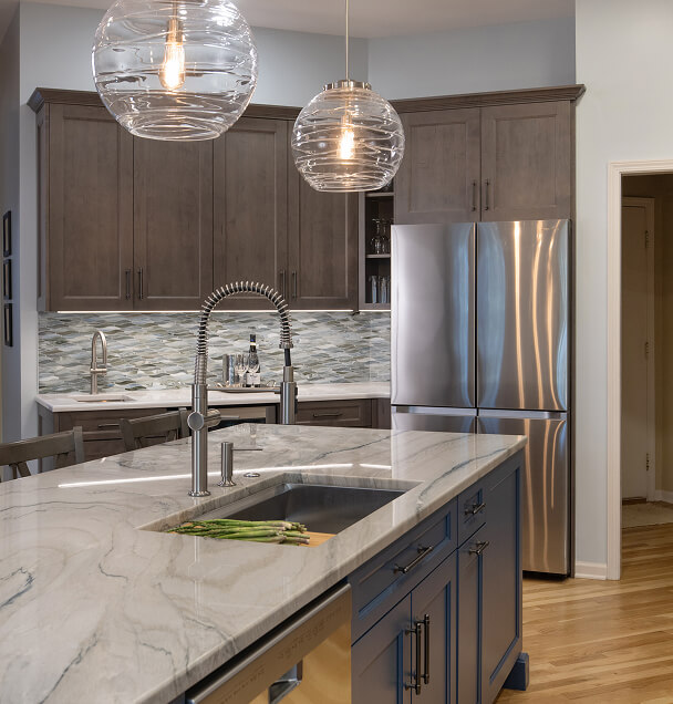 Modern kitchen with gray cabinets, stainless steel appliances, and a marble island with a sink. Elegant pendant lights create a cozy ambiance.