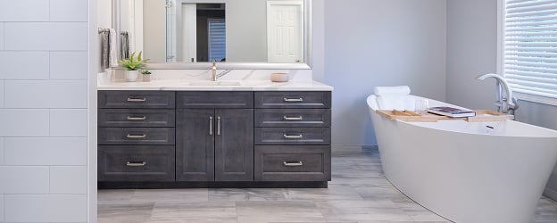 Modern bathroom with grey cabinetry, large mirror, and sleek fittings. A freestanding tub with a wooden tray is near a window, creating a serene atmosphere.