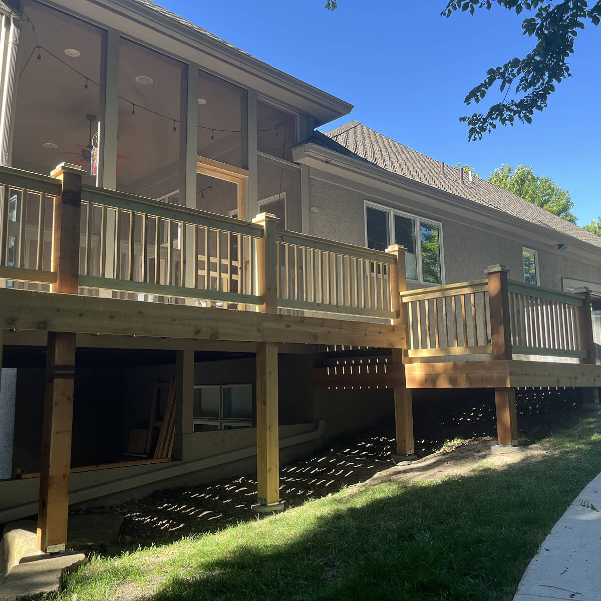 A house with a wooden deck and railing, set against a clear blue sky.
